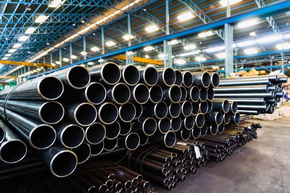 Tubería de acero negro apilada en un almacén industrial.